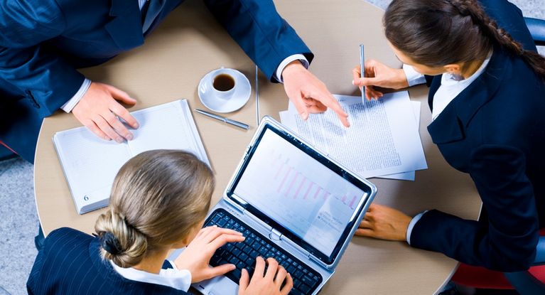 Eine Gruppe junger Managerinnen und Manager sitzt bei einer Besprechung gemeinsam mit einem Laptop am Tisch