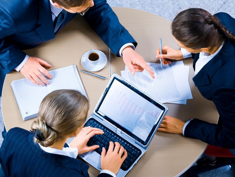 Eine Gruppe junger Managerinnen und Manager sitzt bei einer Besprechung gemeinsam mit einem Laptop am Tisch