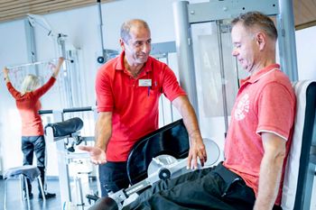 Therapeut berät Patienten, der auf einem Kniebeugetrainer sitzt