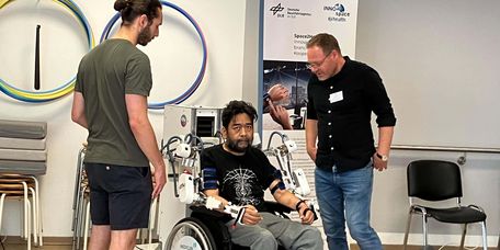Patient bei der Exoskelett-Therapie für die Arme, Therapeuten stehen daneben