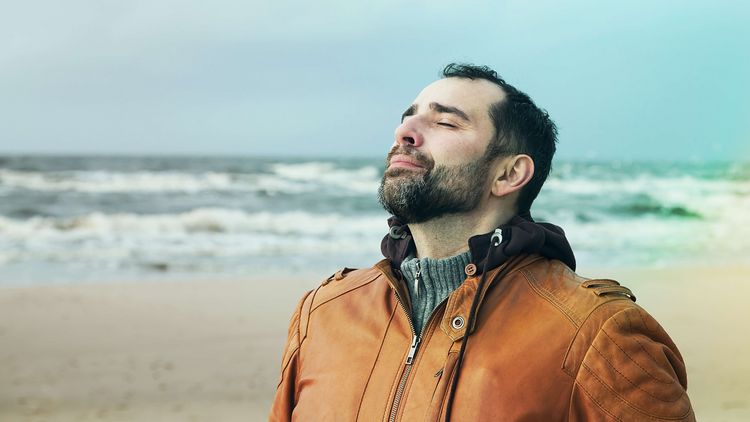 Mann im Jacke atmet frische Meeresluft am Strand
