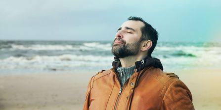 Mann im Jacke atmet frische Meeresluft am Strand