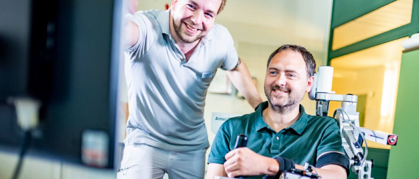 Therapeut unterstützt Patient bei der Armtherapie mit dem Therapiegerät Armeo