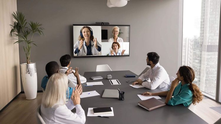 Ärztinnen und Ärzte besprchen sich bei einer hybriden Konferenz vor einem Bildschirm mit weitern Teilnehmerinnen