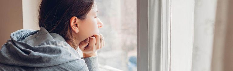 Weibliche Person sieht aus dem Fenster und sieht traurig aus