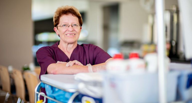 Eine Reinigungskraft lehnt sich auf ihren Wagen mit Putzutensilien und Putzmitteln