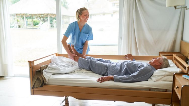Pflegekraft lagert einen Patienten im Bett um