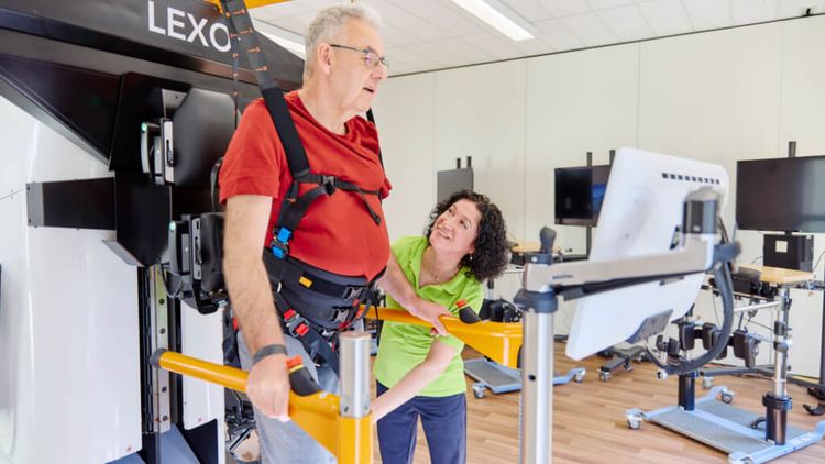 Ein Patient übt mit Unterstützung einer Therapeutin das Laufen mit einem Gangtrainer