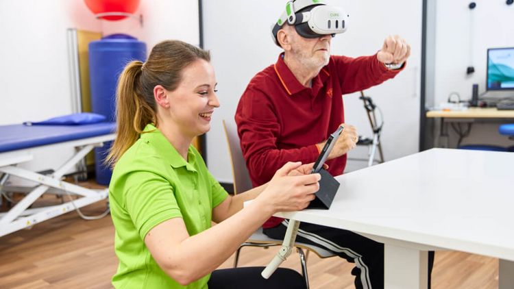 Eine Therapeutin unterstützt bei der VR-Therapie, während ein Patient damit gezielt seine neurokognitiven und motorischen Fährigkeiten schult.