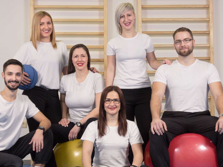 Gruppenbild Therapeutinnen und Therapeuten in weißen T-Shirts mit Bällen vor einer Sprossenwand