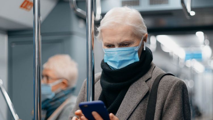 Person fährt mit Maske in der U-Bahn und schaut aufs Handy