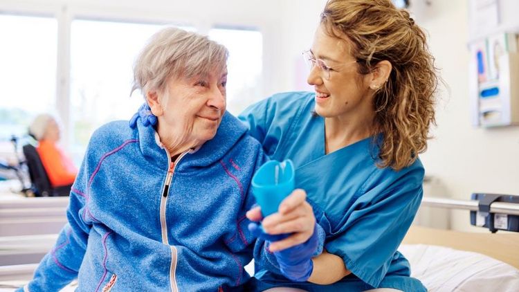 Therapeutin unterstützt eine ältere Patientin im Sitzen beim sicheren Trinken im Rahmen der Schlucktherapie