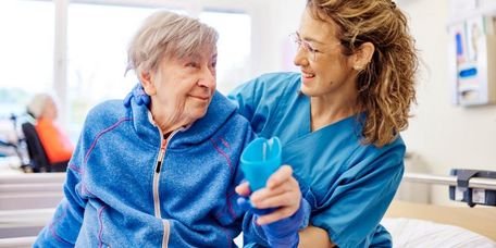 Therapeutin unterstützt eine ältere Patientin im Sitzen beim sicheren Trinken im Rahmen der Schlucktherapie