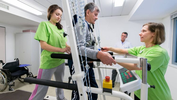 Ein Therapeut und eine Therapeutin helfen einem Patienten auf dem Laufband