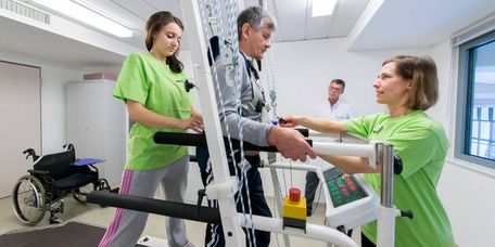Rehabilitation auf dem Laufband Ein Therapeut und eine Therapeutin helfen einem Patienten auf dem Laufband