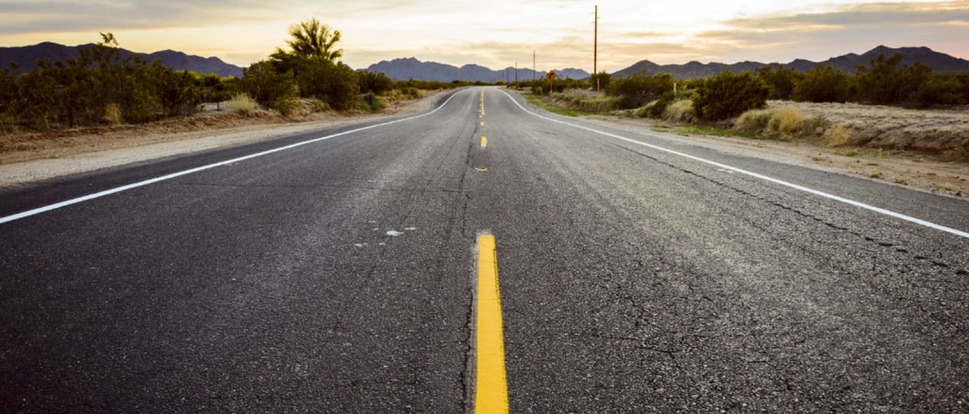 Asphaltierte Straße mit gelbem Mittelstreifen führt durch eine weite steppenähnliche Landschaft
