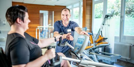 Therapeut erklärt Patientin, wie ein Ergometer funktioniert