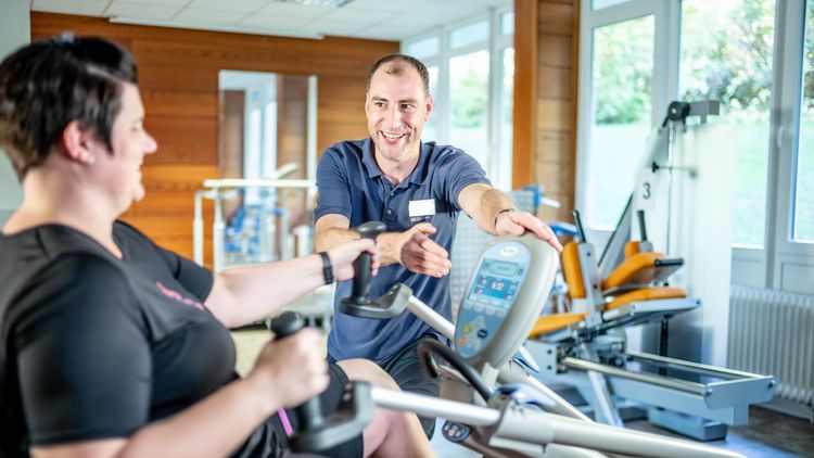 Therapeut erklärt Patientin, wie ein Ergometer funktioniert