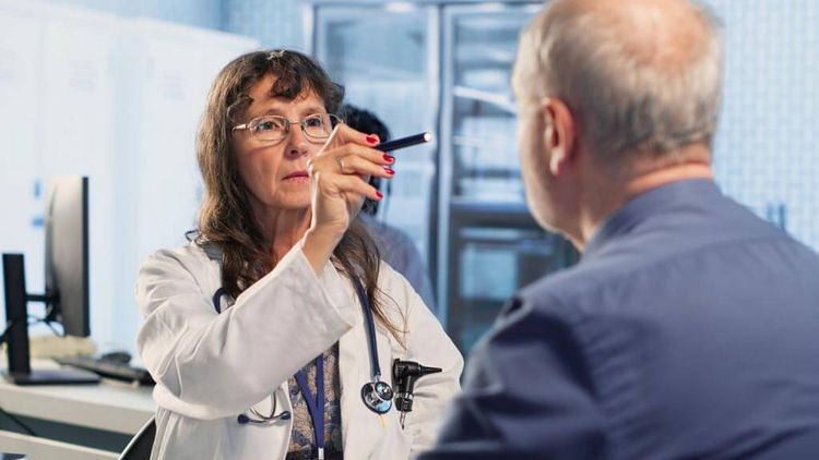 Ärztin untersucht mit einer Leuchte die Augen eines Patienten, neurologische Untersuchung, Diagnostik