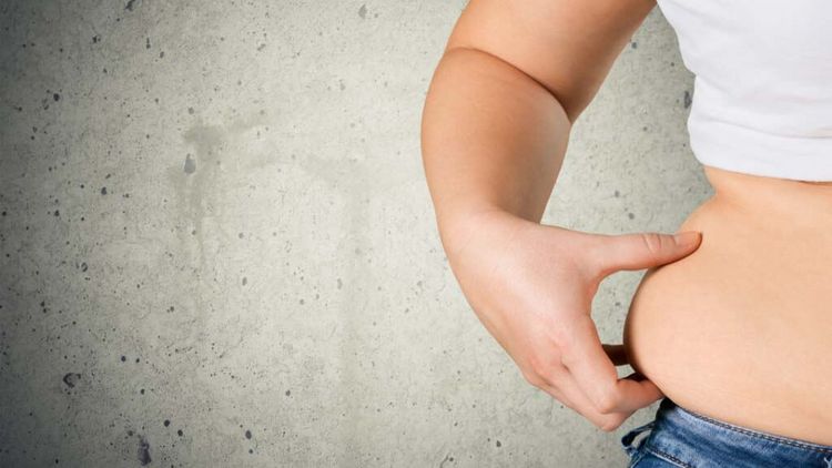 Person greift sich an Speckfalte in Taille