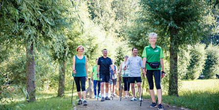 Eine Gruppe Patienten läuft mit Nordicwalkingstöcken und einer Trainerin durch den Park