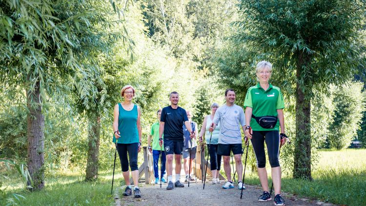 Eine Gruppe Patienten läuft mit Nordicwalkingstöcken und einer Trainerin durch den Park