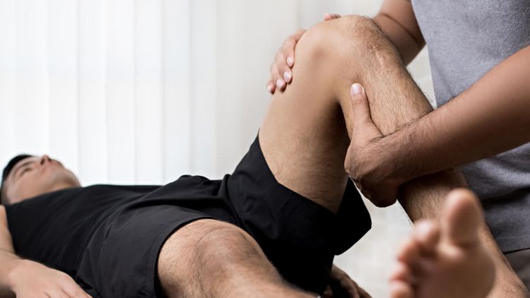 Patient liegt auf einer Therapieliege, während ein Therapeut das Knie behandelt.