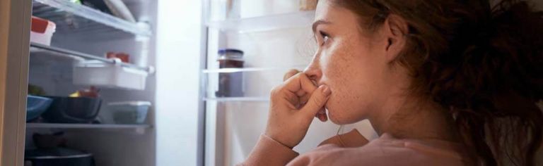 Weibliche Person steht nachts vor dem geöffneten Kühlschrank
