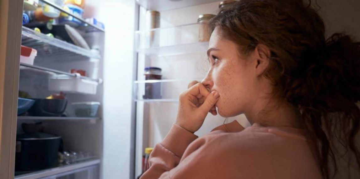Weibliche Person steht nachts vor dem geöffneten Kühlschrank