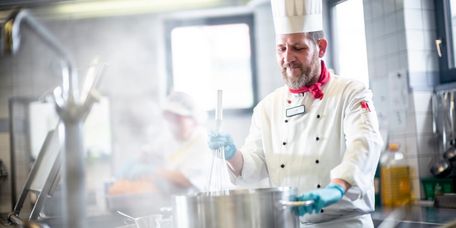 Koch rührt in einer Großküche mit einem Schneebesen in einem Topf