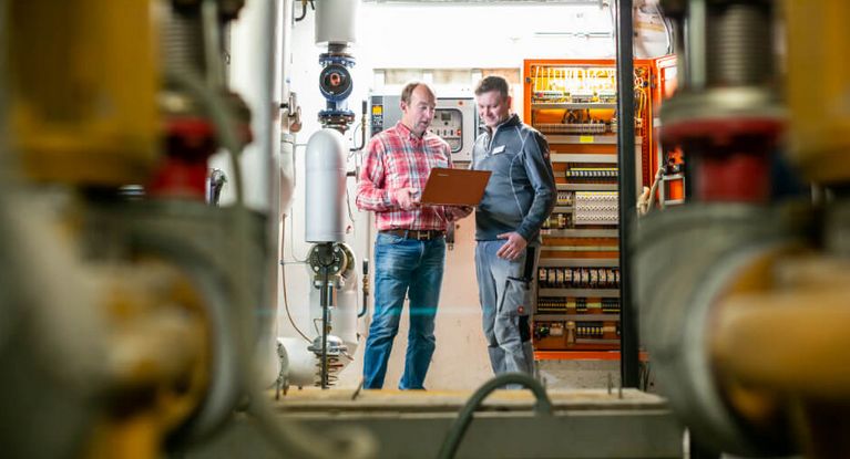 Zwei Haustechniker besprchen im Heizungskeller Messwerte auf einem Laptop