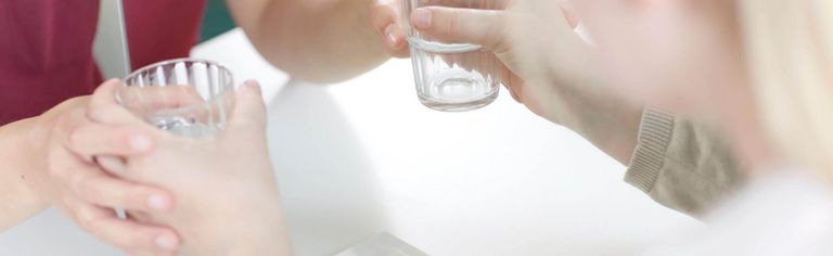 Spiegeltherapie: Patientin sitzt vor dem Spiegel mit einem Glas in der Hand, Therapeutin unterstützt