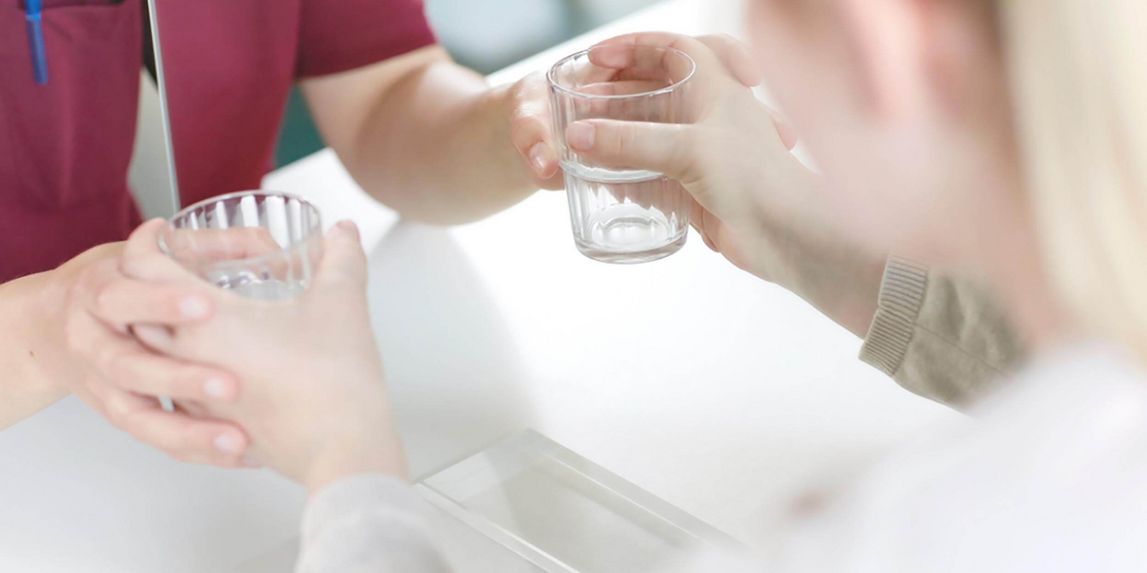 Spiegeltherapie: Patientin sitzt vor dem Spiegel mit einem Glas in der Hand, Therapeutin unterstützt