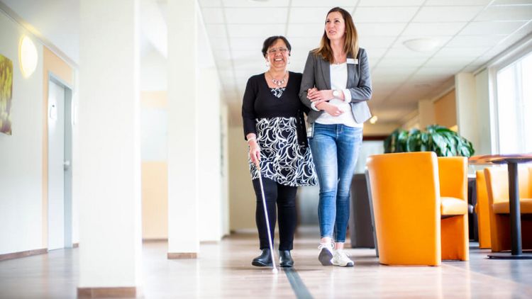 Klinikmitarbeiter gelietet sehbehinderte Patientin, die einen Blindenstock nutzt, durch einen Klinikflur