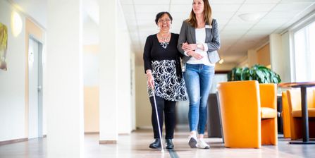 Klinikmitarbeiter gelietet sehbehinderte Patientin, die einen Blindenstock nutzt, durch einen Klinikflur