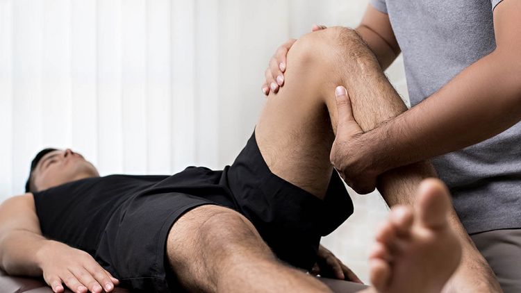 Patient liegt auf einer Therapieliege, während ein Therapeut das Knie behandelt.