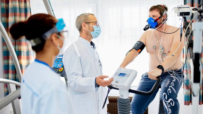 Pflegekraft und Arzt sprechen mit Patienten beim Lungenfunktionstest auf dem Ergometer