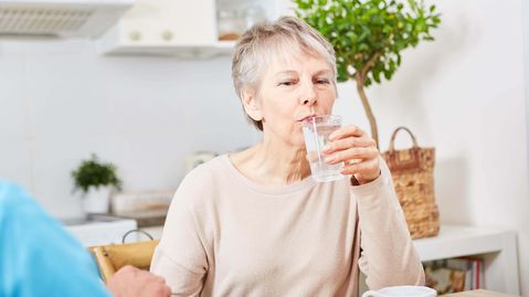 Ältere Frau trinkt aus einem Wasserglas