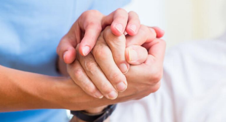 Pflegerin hält die Hand eines älteren Patienten