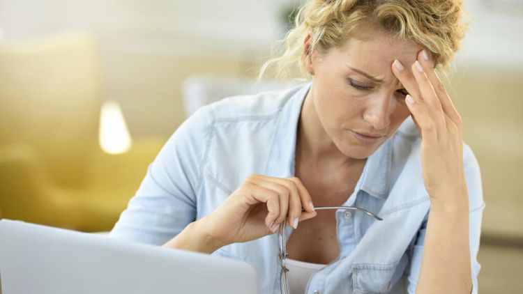 Eine erschöpfte Frau vor einem Laptop hält ihre Hand an der Stirn
