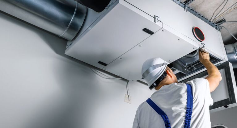 Ein Mechaniker mit Bauhelm repariert über Kopf einen Lüftungsschacht