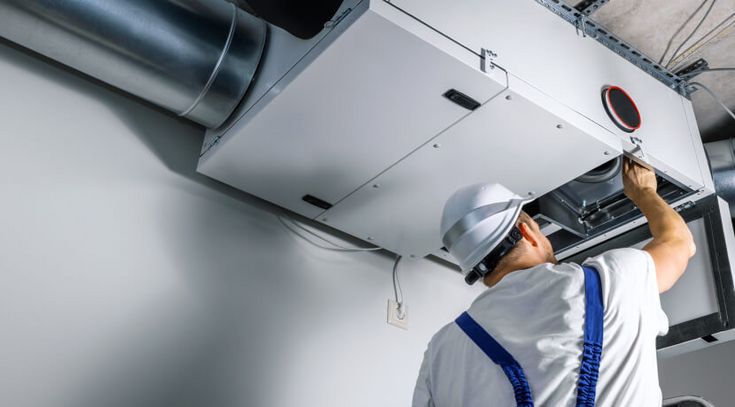 Ein Mechaniker mit Bauhelm repariert über Kopf einen Lüftungsschacht