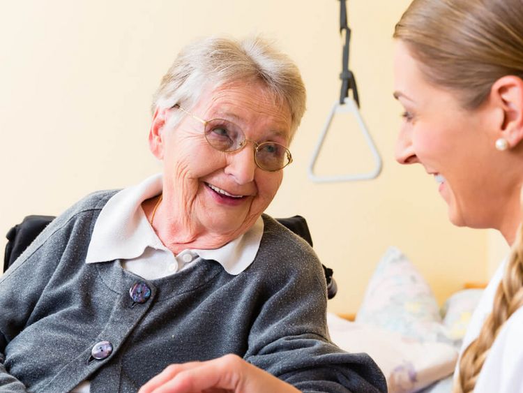Pflegekraft behandelt die Hand einer älteren Person und beide lächeln sich an.