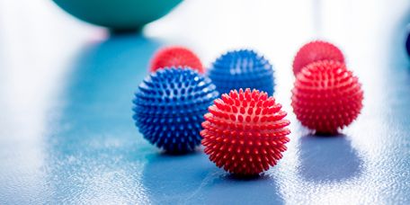Praxis_fuer_Physiotherapie_verkaufen Rote und blaue Igelbälle liegen vor einem grünen Pezziball