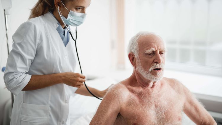 Ärztin in weißem Kittel untersucht älteren Patienten mit einem Stethoskop am Rücken