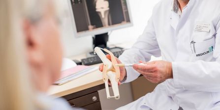 Arzt erläutert Patienten die Funktion des Kniegelenks an einem Knochenmodell