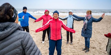 Therapeutin und Patientengruppe wärmen sich im Herbst am Strand mit Gymnastik auf