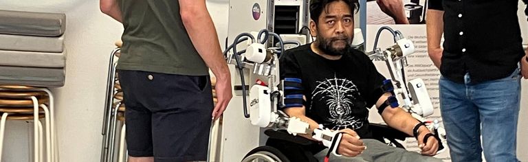 Patient sitzt im Rollstuhl, Arme im Exoskelett, robotikgestützte Therapie