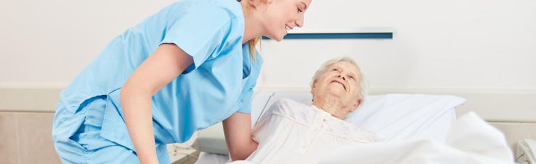 Pflegekraft bettet Seniorin im Krankenbett