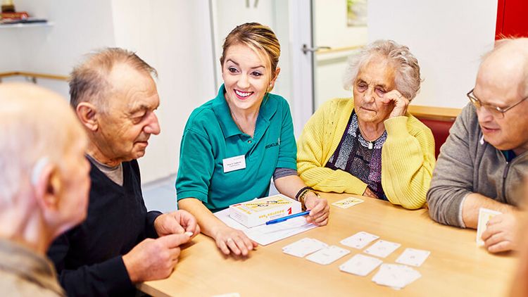 Ältere Patienten und Therapeutin spielen Karten